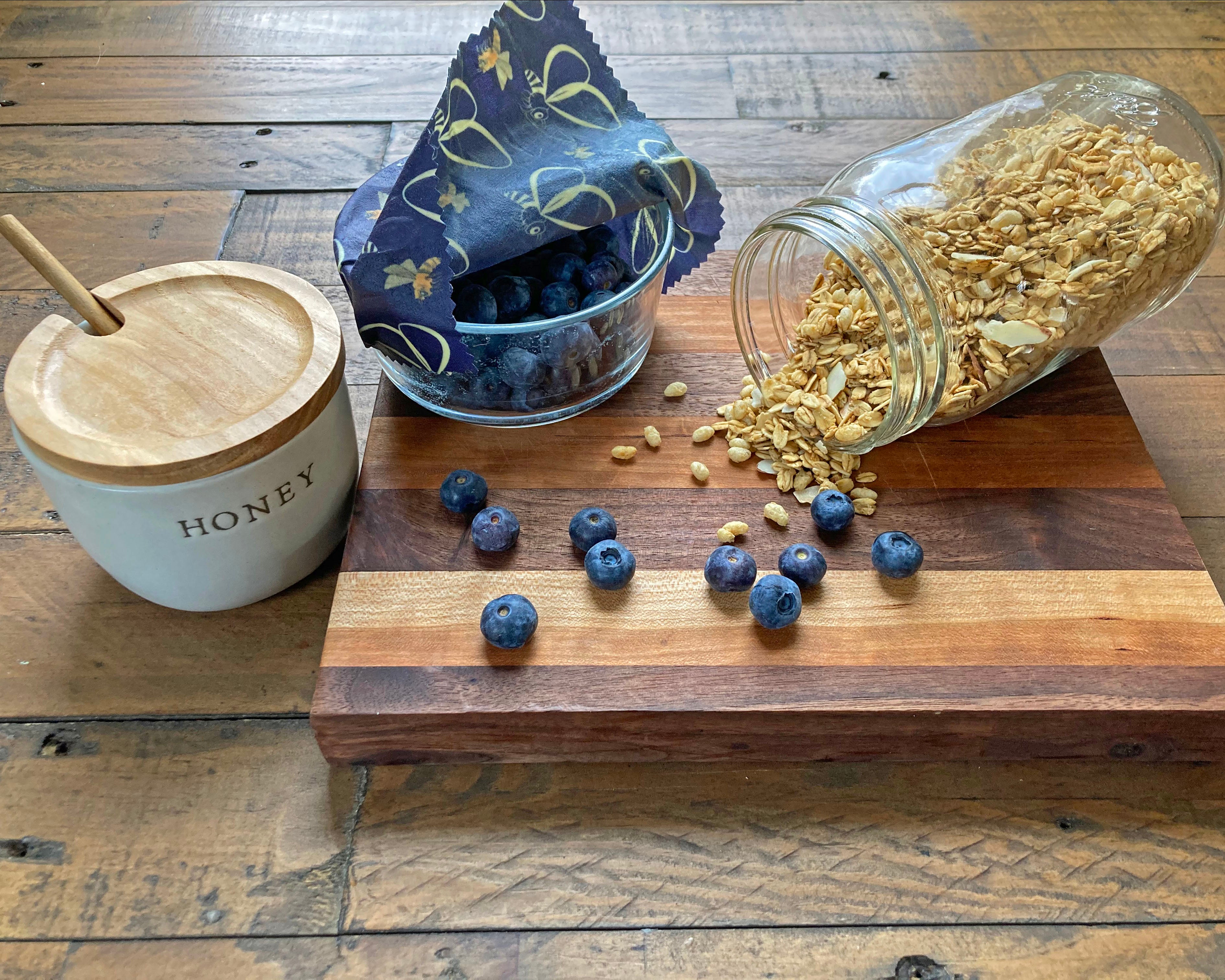 Wooden cutting board with honey, blueberries, and granola on a wooden surface